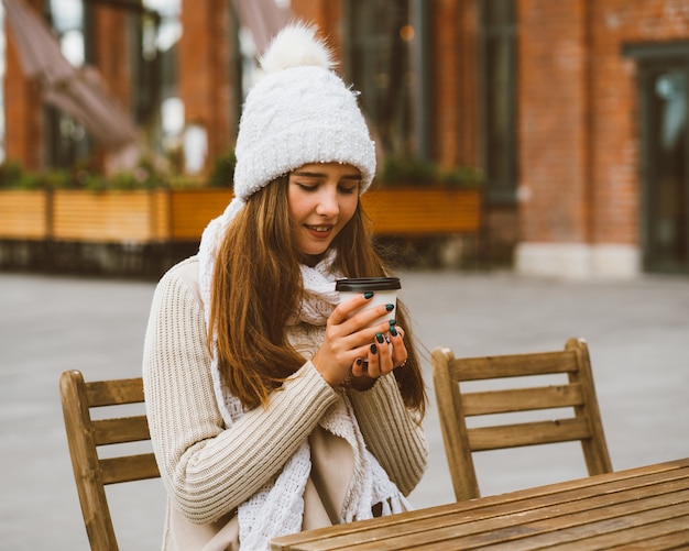 Beautiful young girl drinking coffee, tea from plastic mug in autumn, winter.