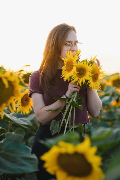 Bella ragazza che gode della natura sul campo dei girasoli al tramonto