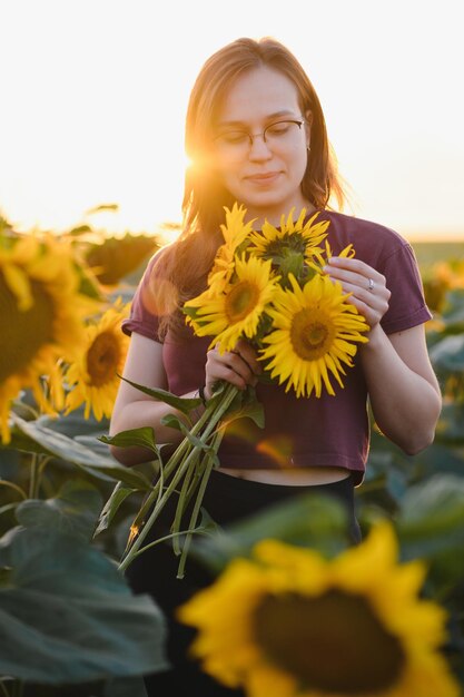 Beautiful young girl enjoying nature on the field of sunflowers at sunset