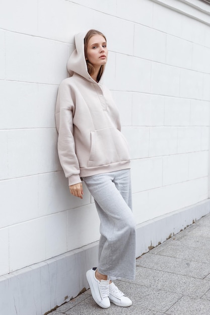 Beautiful young girl in fashionable biege hoodie and pants on light background Walking on the street