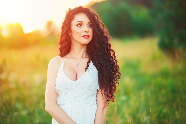 Красивая молодая девушка в поле в белом платье имеет красивые длинные волосы