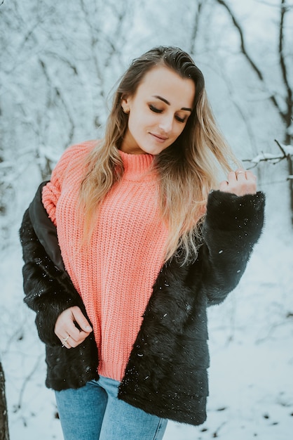 Bella ragazza in un maglione voluminoso rosa cappotto di pelliccia e jeans in una foresta di inverno nevoso freddo