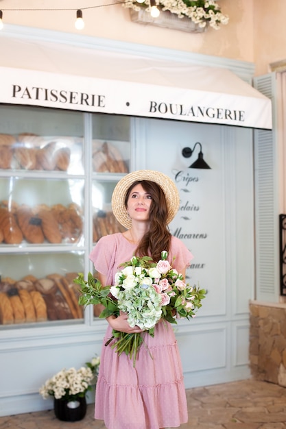 Beautiful young girl in a gently pink dress holding a bouquet of roses in one hand at bakery