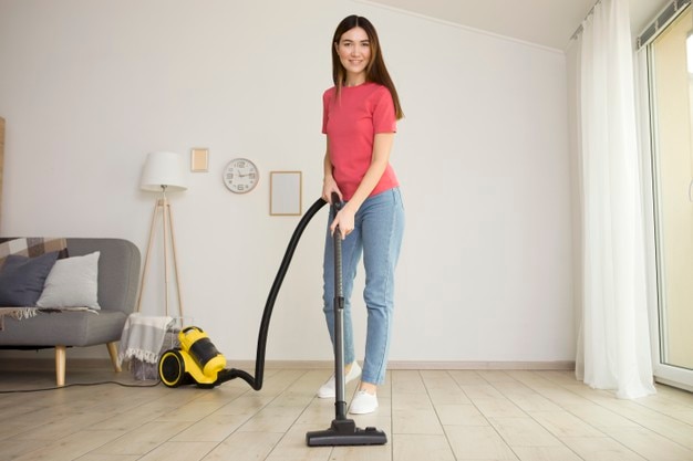 Beautiful young girl in a good mood makes house cleaning with a vacuum cleaner