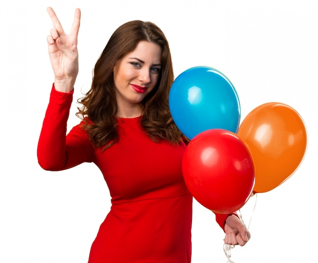 Beautiful young girl holding balloons and making victory gesture