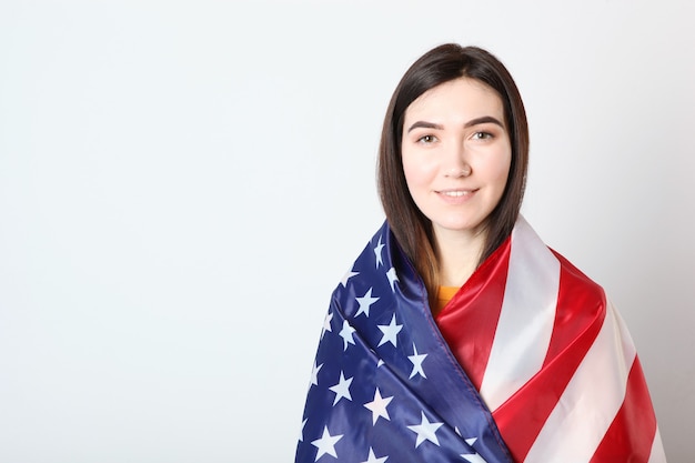 Beautiful young girl holding the flag of america on a colored background