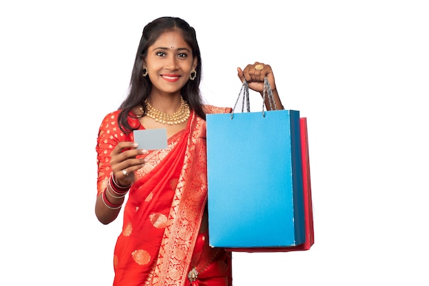 Красивая молодая девушка держит и позирует с сумками для покупок и кредитной или дебетовой картой на белом фоне