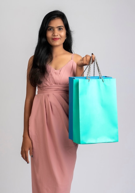 Beautiful young girl holding and posing with shopping bags on a grey wall