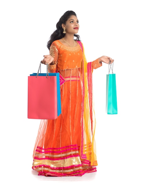 Beautiful young girl holding shopping bags while wearing traditional ethnic wear on white