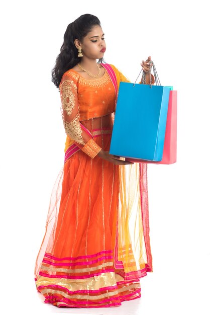 Beautiful young girl holding shopping bags while wearing traditional ethnic wear on white