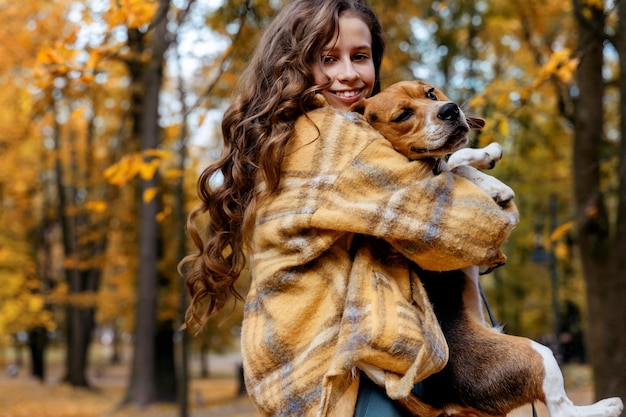 Beautiful young girl hugging with beagle dog in autumn park.