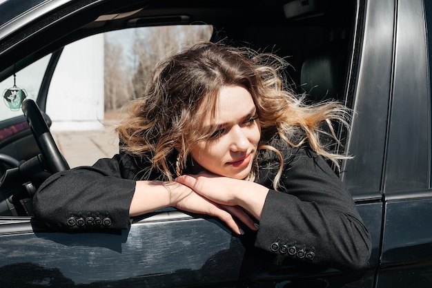 사진 검은 차에 아름 다운, 어린 소녀입니다. 소녀는 운전대 뒤에 앉아 창 밖을 내다봅니다.