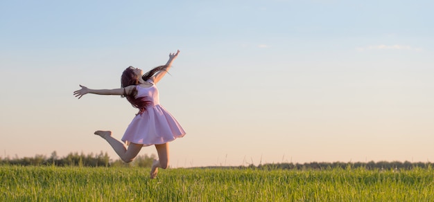 사진 필드에서 점프 핑크 드레스에 아름 다운 젊은 여자