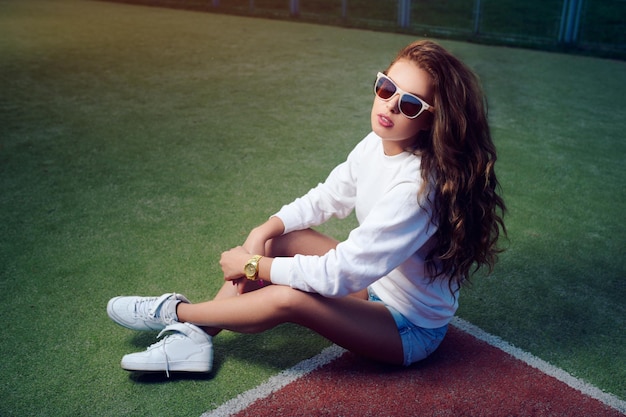 사진 테니스 코트에서 선글라스를 쓴 아름다운 소녀 아름다운 건강한 머리 데님 반바지 흰색 운동화