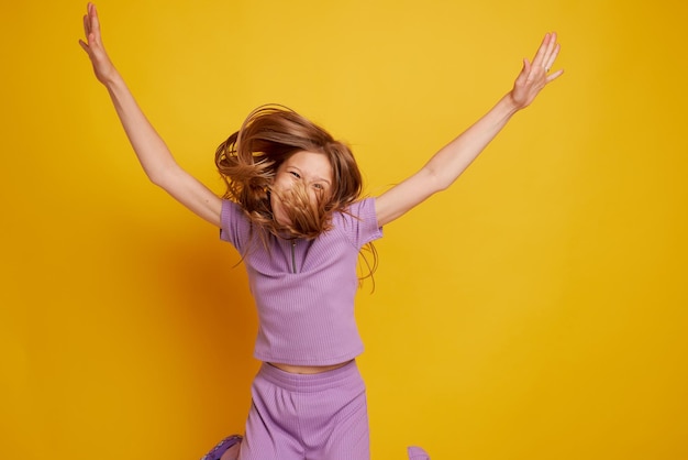 A beautiful young girl is dancing laughing and having fun on a clean yellow background