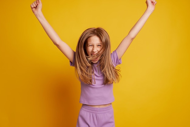 A beautiful young girl is dancing laughing and having fun on a clean yellow background