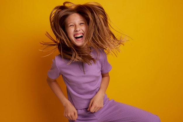 A beautiful young girl is dancing laughing and having fun on a clean yellow background