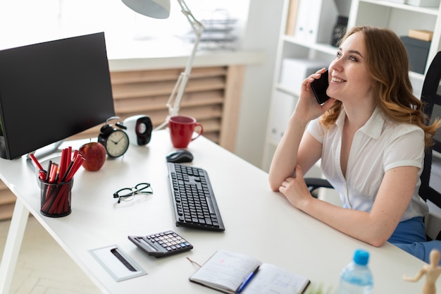 Beautiful young girl is sitting in the office and talking on the phone.