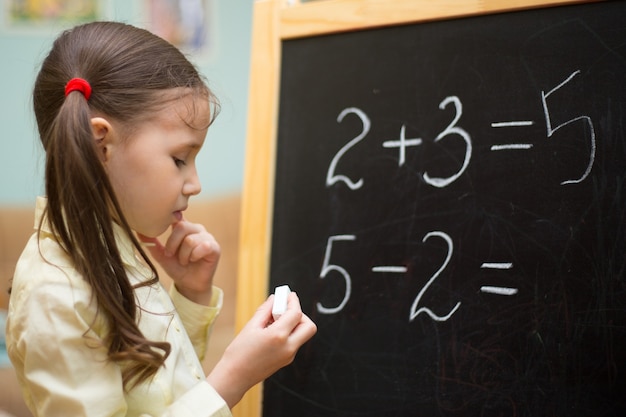 Photo beautiful young girl is teaching at home on blackboard