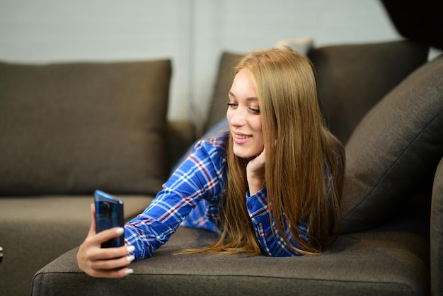 Beautiful young girl laying on bad and making happy selfi