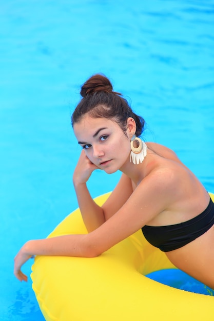 Photo a beautiful young girl lies on an inflatable mattress in the summer water park. girl swims in the summer pool.