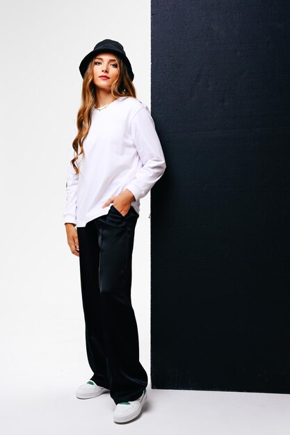 A beautiful young girl looks forward confidently A model with long hair and blue eyes in a hat against a black and white wall with copy space