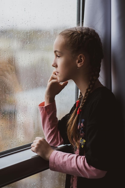 A beautiful young girl looks out the window with rain and\
dreams rain autumn atmosphere