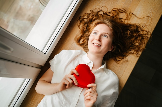 Beautiful young girl lying by the window with a gift for Valentines Day