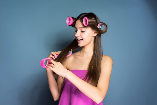 Beautiful young girl makes a fashionable hairstyle with curlers and combs