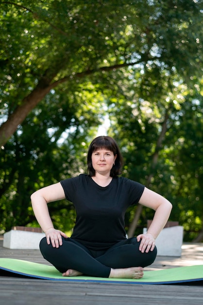 Beautiful young girl meditates in the park sitting on a green yoga mat. Healthy lifestyle. Lotus position.