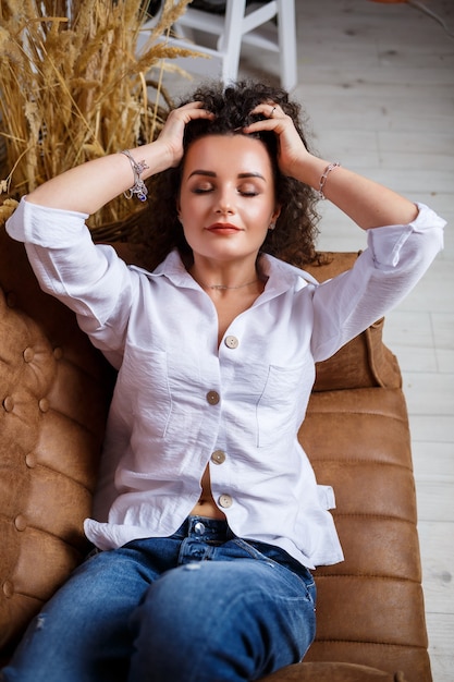 Foto bello modello della ragazza con la posa dei riccioli. indossa una camicia bianca e jeans.