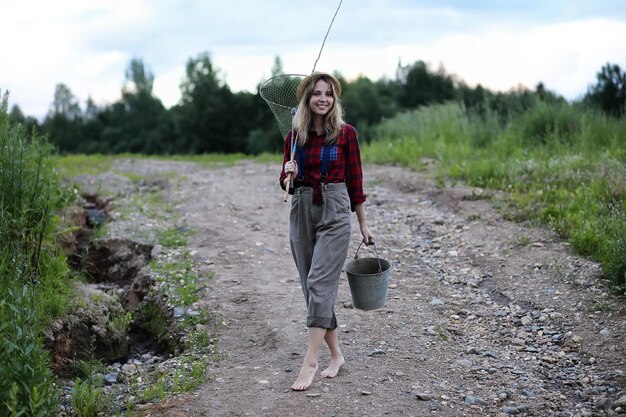 Beautiful young girl on the nature by the river with a fishing rod