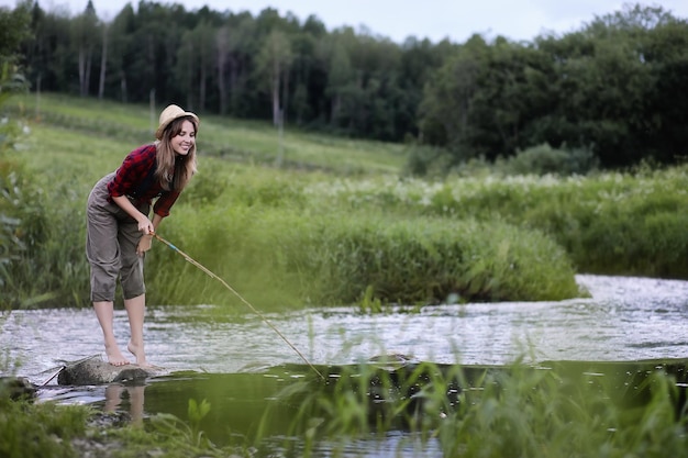 Beautiful young girl on the nature by the river with a fishing rod