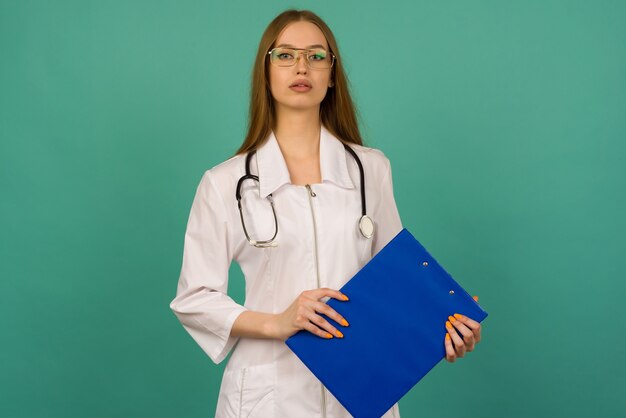 Beautiful young girl nurse or trainee doctor with blue folder and statoscope on a blue space