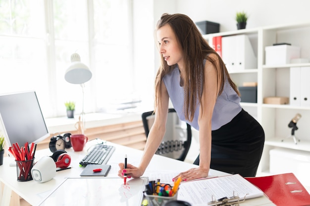 Beautiful Young girl in an office is standing near a table and draws a marker on a magnetic board.