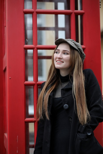 Beautiful young girl in a phone booth. The girl is talking on the phone from the payphone. English telephone booth in the street and a woman talking on the phone.