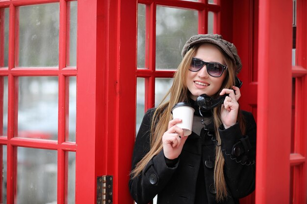 Beautiful young girl in a phone booth The girl is talking on the phone from the payphone English telephone booth in the street and a woman talking on phone