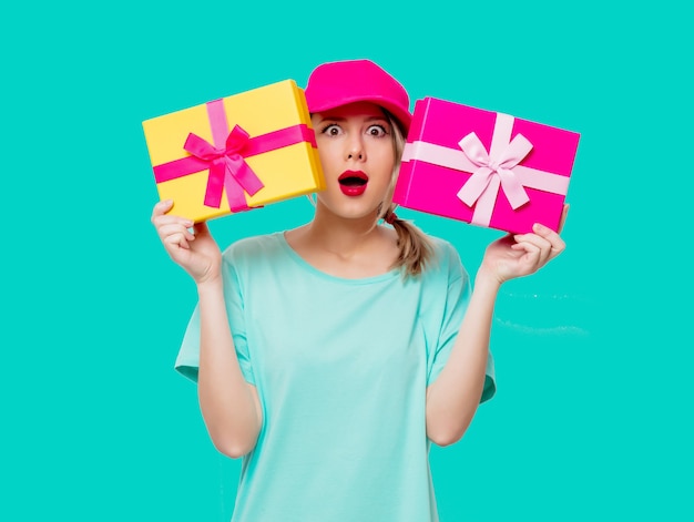 Beautiful young girl in pink cap and blue t-shirt with holiday present boxes on green background.