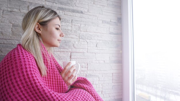 一杯のコーヒーとピンクの格子縞の美しい少女。バルコニーの若い女性。居心地の良い朝食のために一杯のコーヒーのために休んでください。