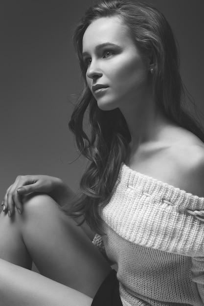 Beautiful young girl posing and sitting on white background. blonde in a white sweater.