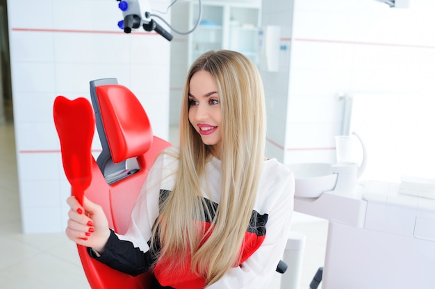 Beautiful young girl in red dental chair with dental mirror