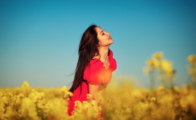 Bella ragazza in un vestito rosso che posa in un campo con canola