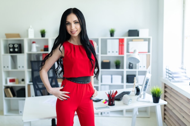 Beautiful young girl in a red suit is standing in the office. 