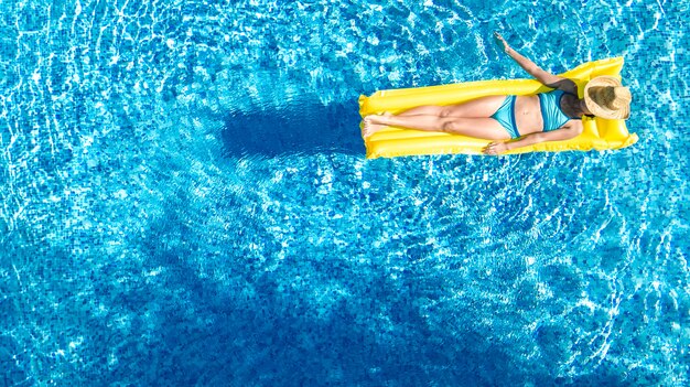 Beautiful young girl relaxing in swimming pool, swims on inflatable mattress and has fun in water on family vacation, tropical holiday resort, aerial drone view from above