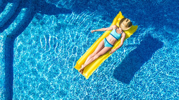スイミングプールでリラックスした美しい少女、膨脹可能なマットレスで泳ぐし、家族での休暇、トロピカルホリデーリゾート、上から空中ドローンビューで水中で楽しい時を過す