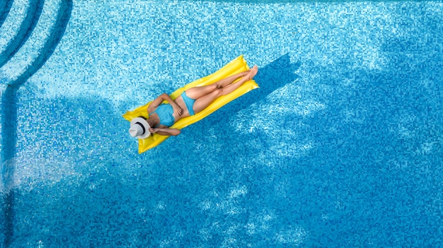 Bella ragazza che si rilassa in piscina, nuota sul materasso gonfiabile e si diverte in acqua in vacanza con la famiglia, località di villeggiatura tropicale, vista aerea del drone dall'alto