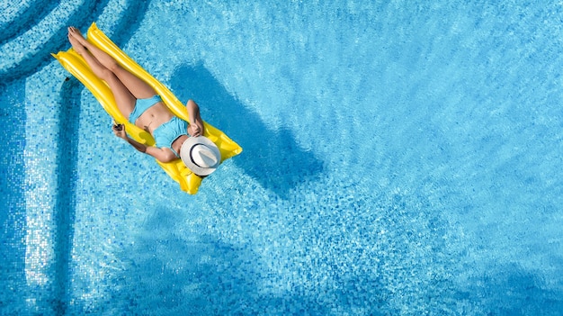 Beautiful young girl relaxing in swimming pool, woman on inflatable mattress, aerial view