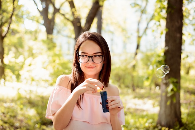 Bella ragazza in una luminosa giornata di sole divertendosi con le bolle nel parco