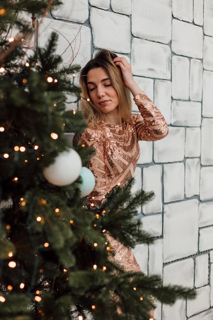 A beautiful young girl in a short sexy dress stands near the Christmas tree