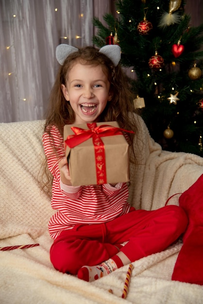 美しい若い女の子がクリスマスの新年の贈り物を持ってソファに座っています